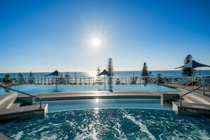 A pool with a view of the ocean, surrounded by lounge chairs and umbrellas. - Halo by Aryve | Surfers Paradise (Surfers Paradise)