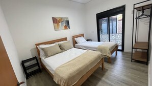 Quarto de hotel com duas camas de madeira, um quadro na parede e uma varanda com guarda-corpo de metal.