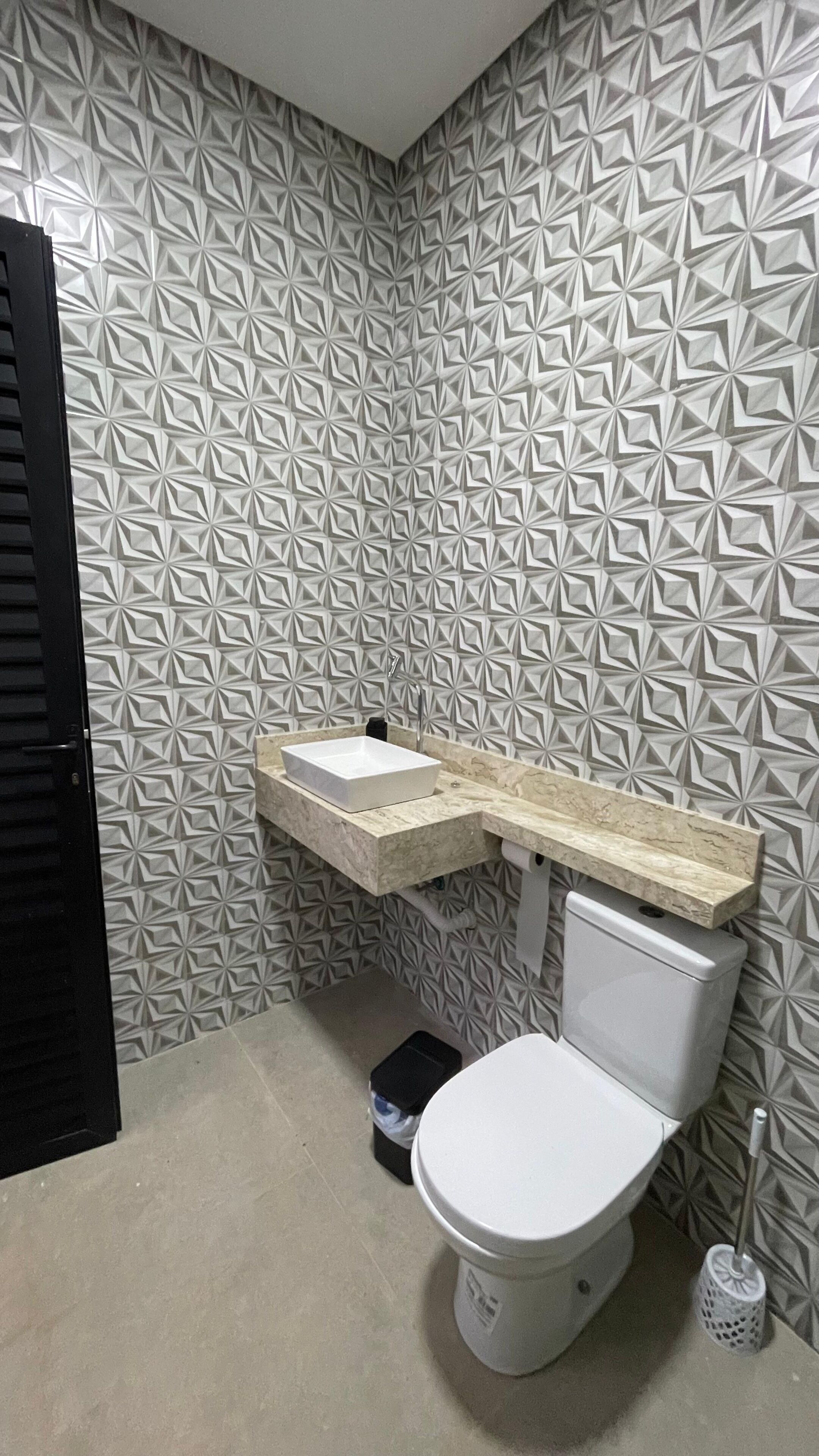 Casa de banho com sanita branca, lavatório com bancada de mármore e parede com padrão.