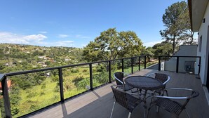 Varanda com mesa e cadeiras, com vista para uma paisagem verde e edifícios ao longe.