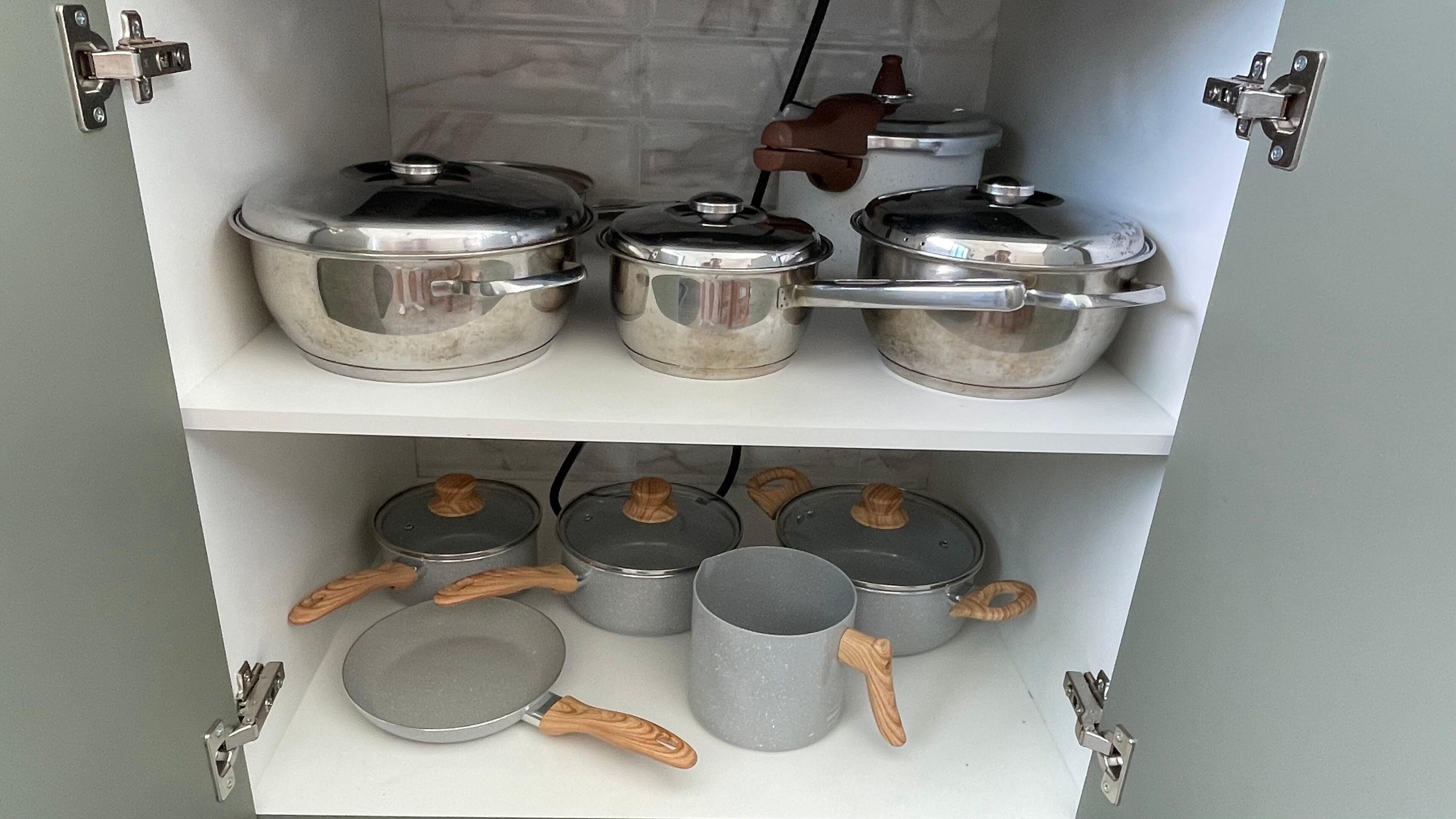 A kitchen cabinet with stainless steel cookware and wooden-handled utensils.