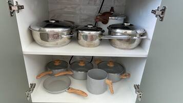 A kitchen cabinet with stainless steel cookware and wooden-handled utensils.