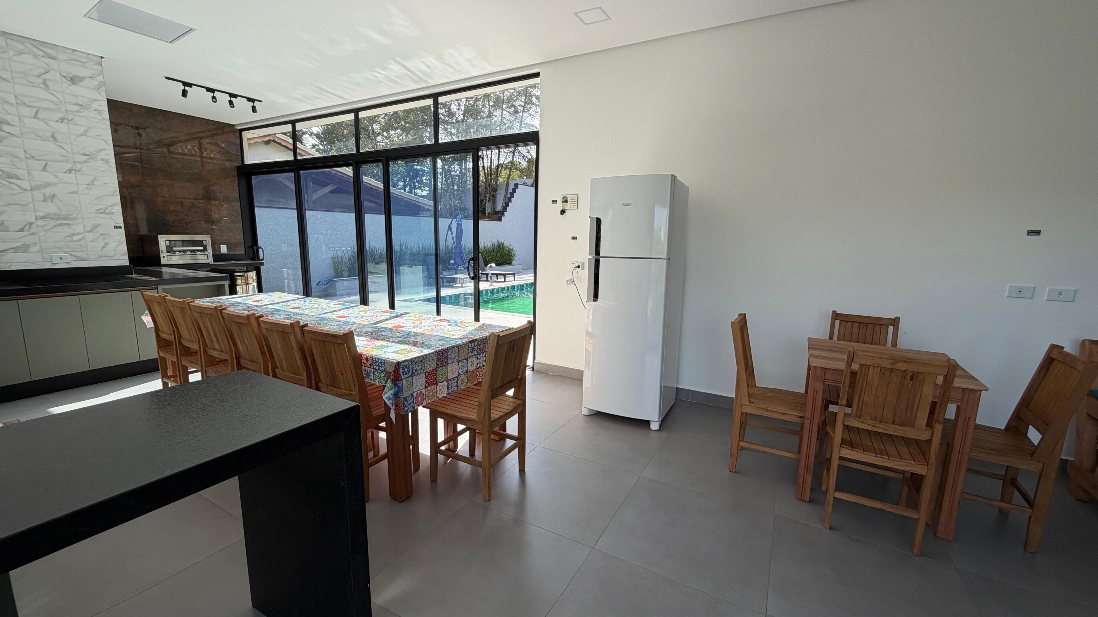 A modern kitchen with a dining area, large windows, and a view of a swimming pool.