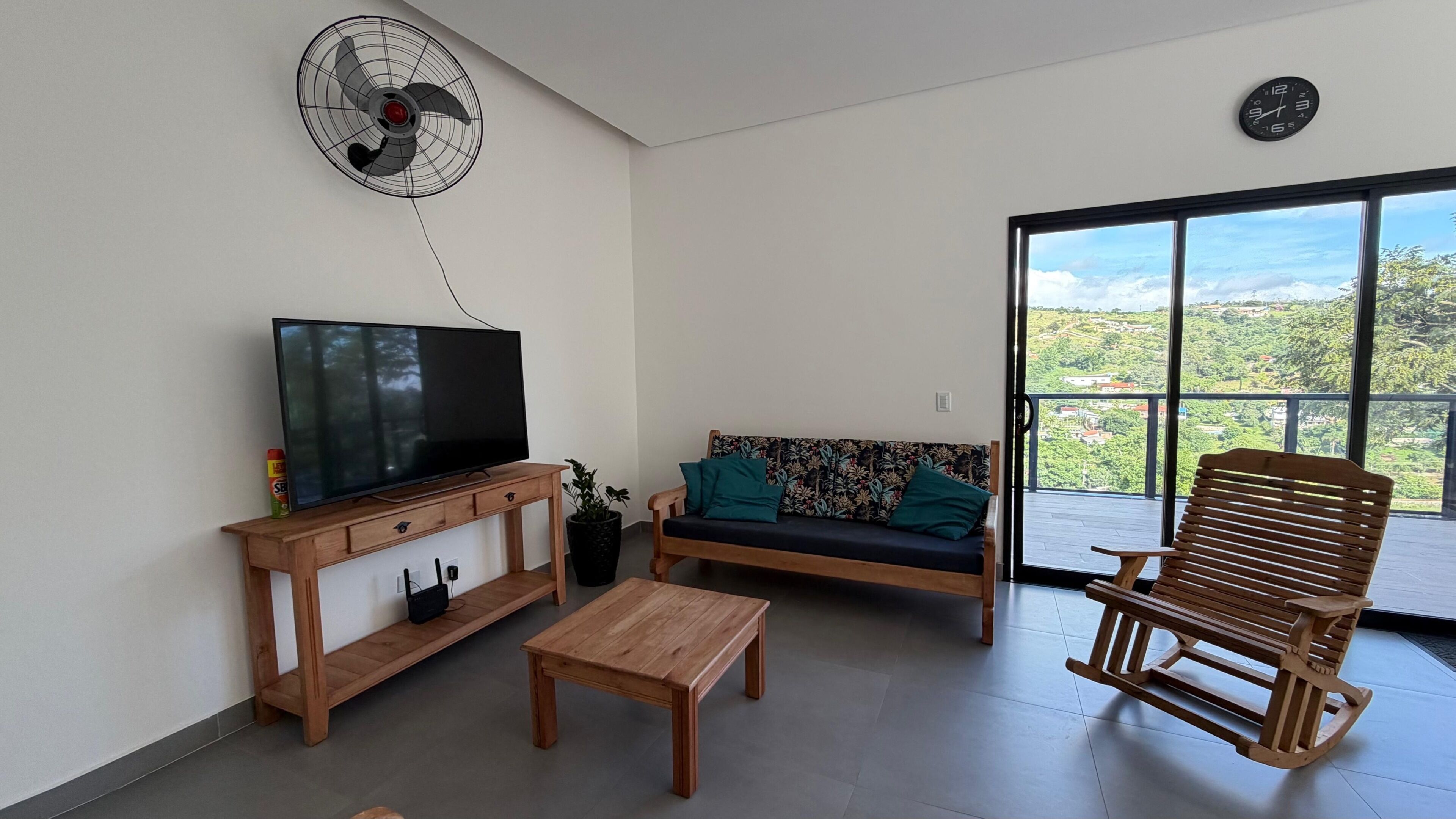 A living room with a TV, wooden furniture, a fan, and a view through a glass door.