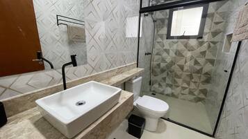 Casa de banho com lavatório branco, sanita e zona de duche.