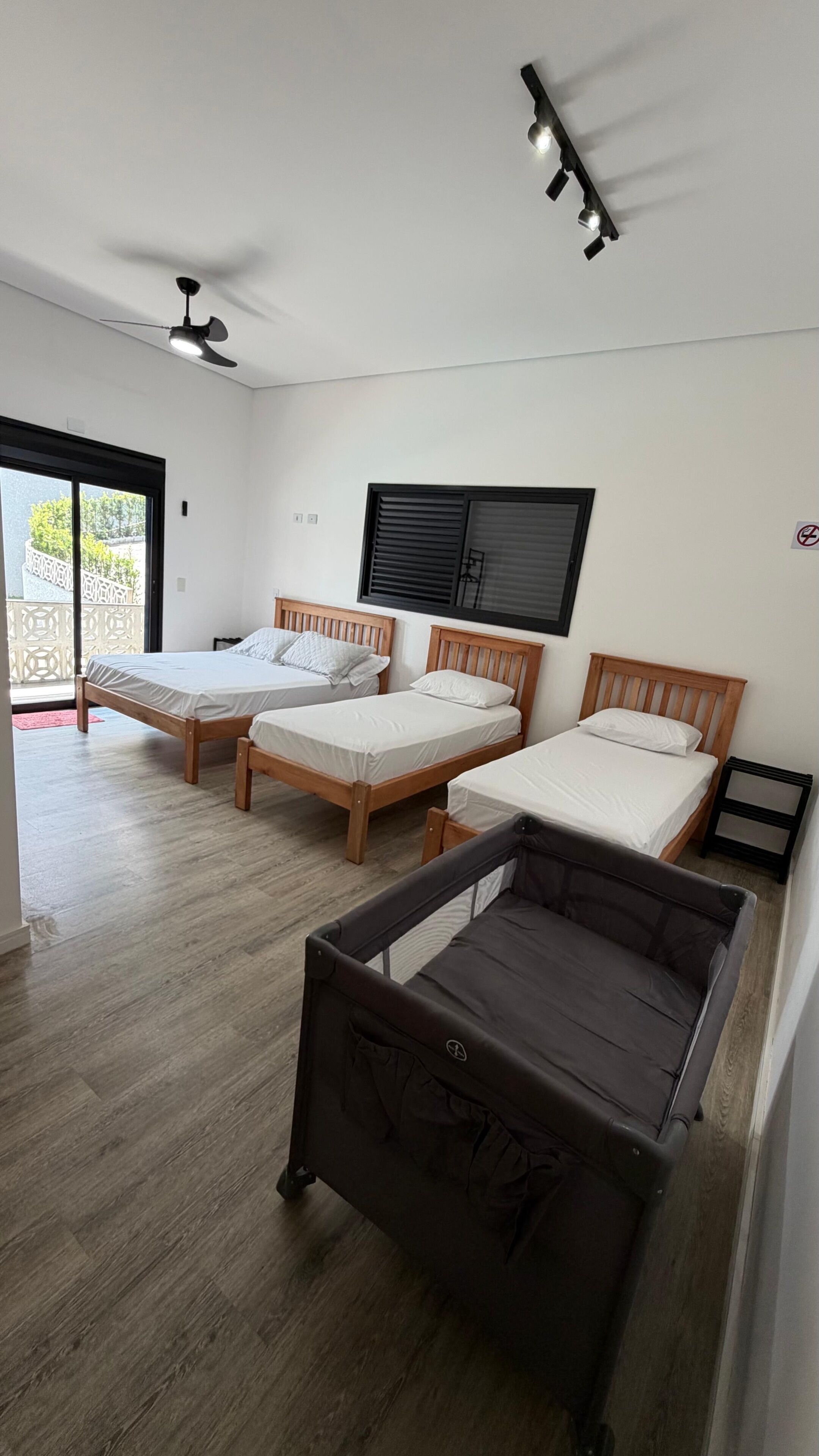 Quarto com três camas de madeira, um ventilador de teto e uma janela com persianas.
