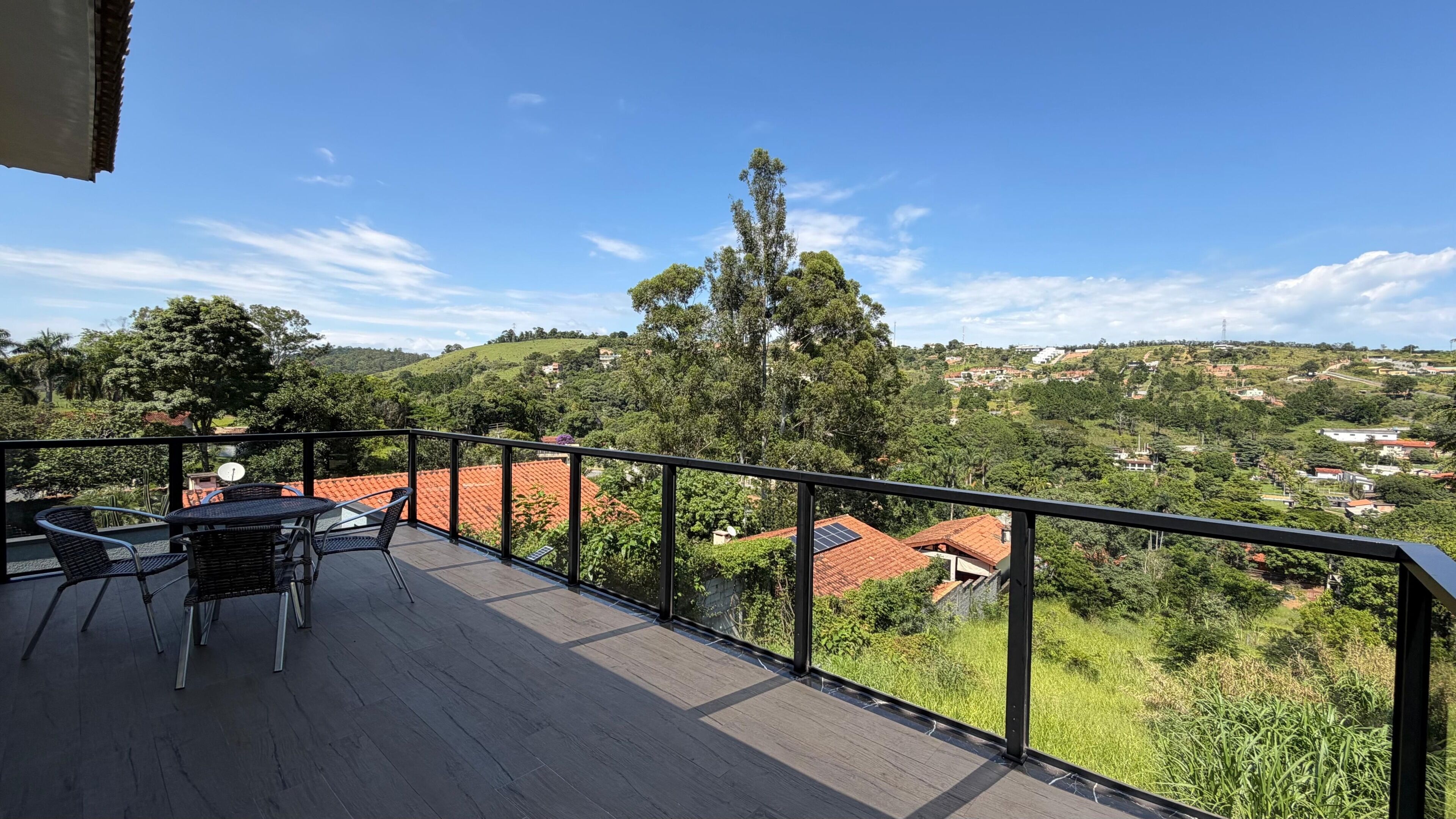 En balkon med et bord og stole, der giver udsigt over et bakket landskab med huse og grønt.