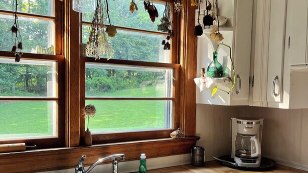 A kitchen with a double sink, wooden window frames, hanging dried flowers, and a coffee maker on the counter. - Charming 2-bedroom house in peaceful Cunningham (Cunningham)