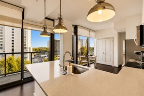 A modern kitchen with a large island, stainless steel appliances, and a view of the city through large windows. - Buckhead Luxury 1BR - Lenox City View - Free Parking (Atlanta)