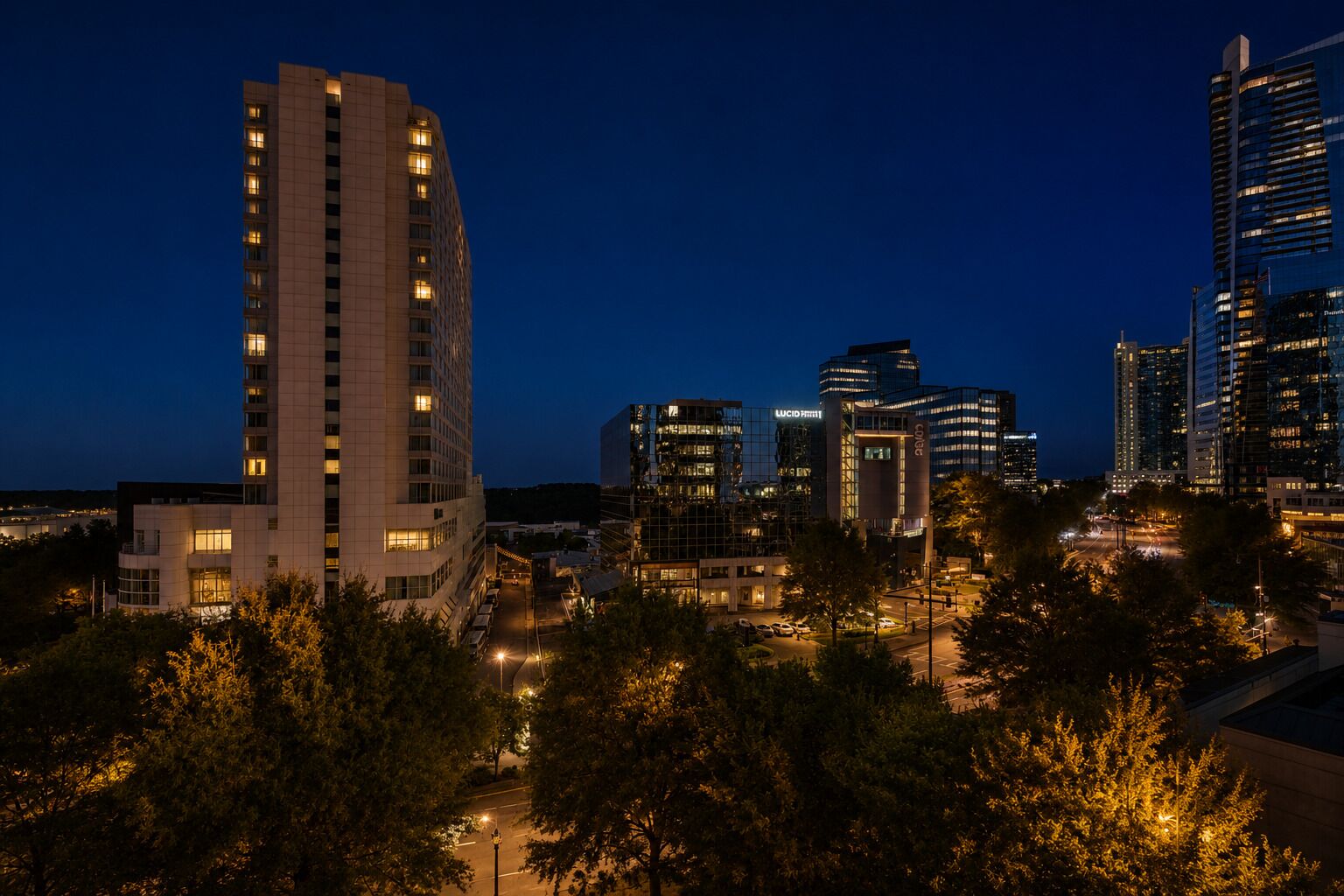 A nighttime cityscape with modern buildings, including a prominent high-rise hotel and several other commercial structures.