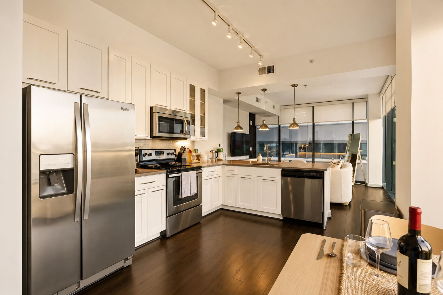 A modern kitchen with stainless steel appliances, white cabinetry, and a large island with a sink and seating.