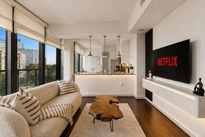 A modern living room with a sofa, a coffee table, and a TV mounted on the wall displaying 'NETFLIX'. - Buckhead Luxury 1BR - Lenox City View - Free Parking (Atlanta)