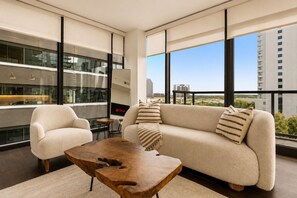 Ein modernes Wohnzimmer mit Sofa, Sessel und Couchtisch, großen Fenstern mit Blick auf die Stadt und einem Netflix-Schild.