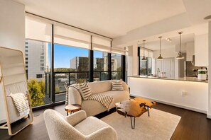 A modern living room with a sofa, chairs, and a small table. There is a large window with a view of buildings and a balcony. - Buckhead Luxury 1BR - Lenox City View - Free Parking (Atlanta)