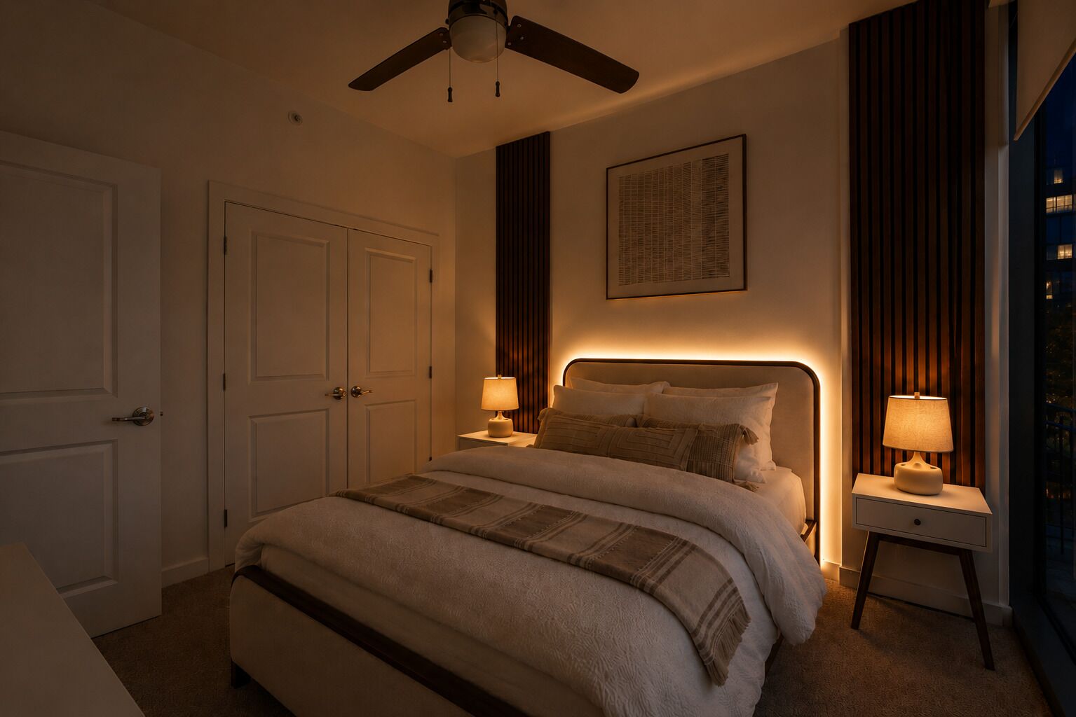 A bedroom with a bed, two bedside tables with lamps, a ceiling fan, a door, and a framed picture on the wall.