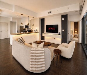 A modern living room with a sofa, a coffee table, and a TV mounted on the wall. - Buckhead Luxury 1BR - Lenox City View - Free Parking (Atlanta)