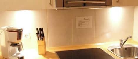 Et køkken med indbygget ovn, kaffemaskine, vask og bestikbakke.