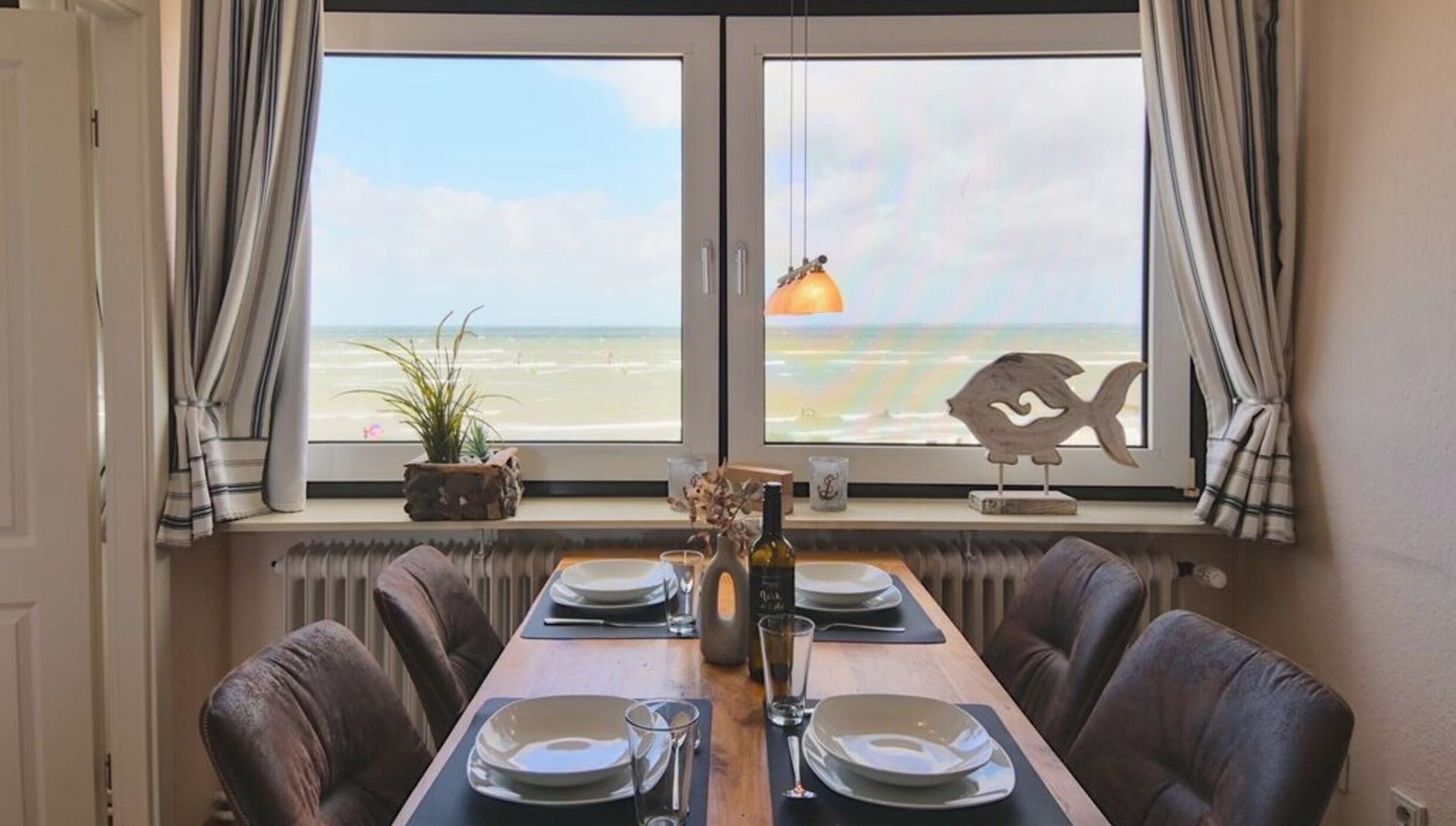 A dining area with a view of the beach, a table set for two, and a decorative fish ornament.