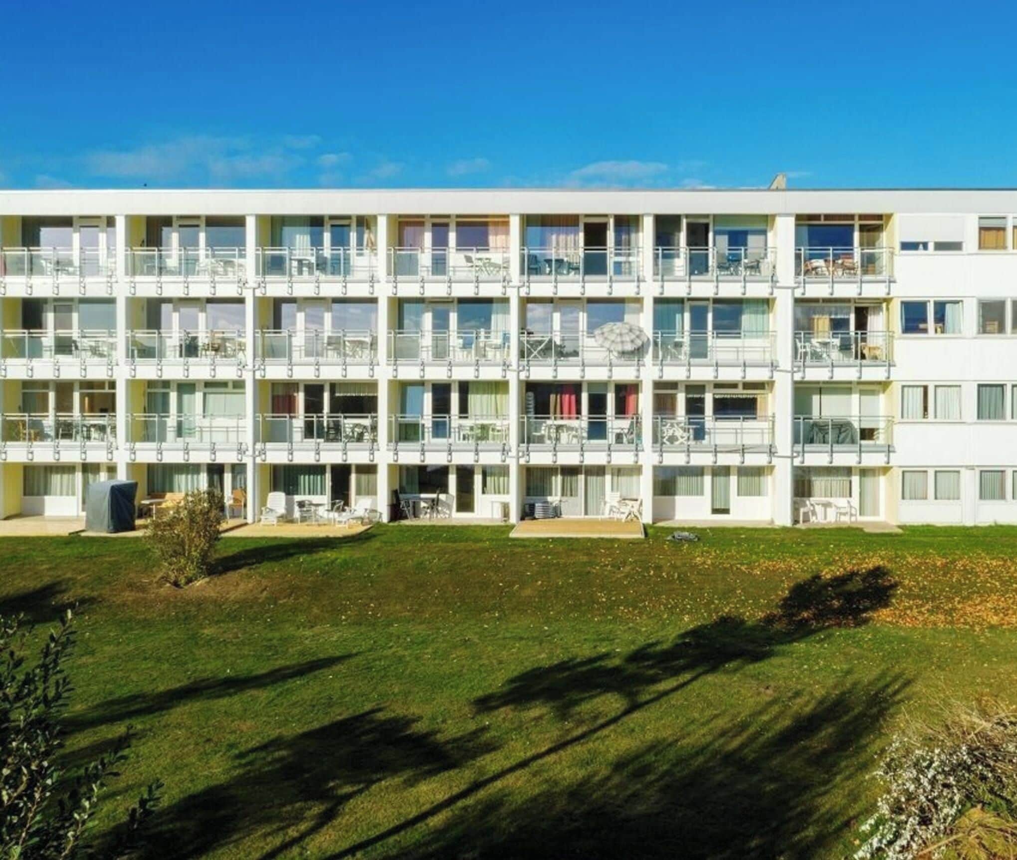 A multi-story hotel with balconies, outdoor seating, and a well-maintained lawn.