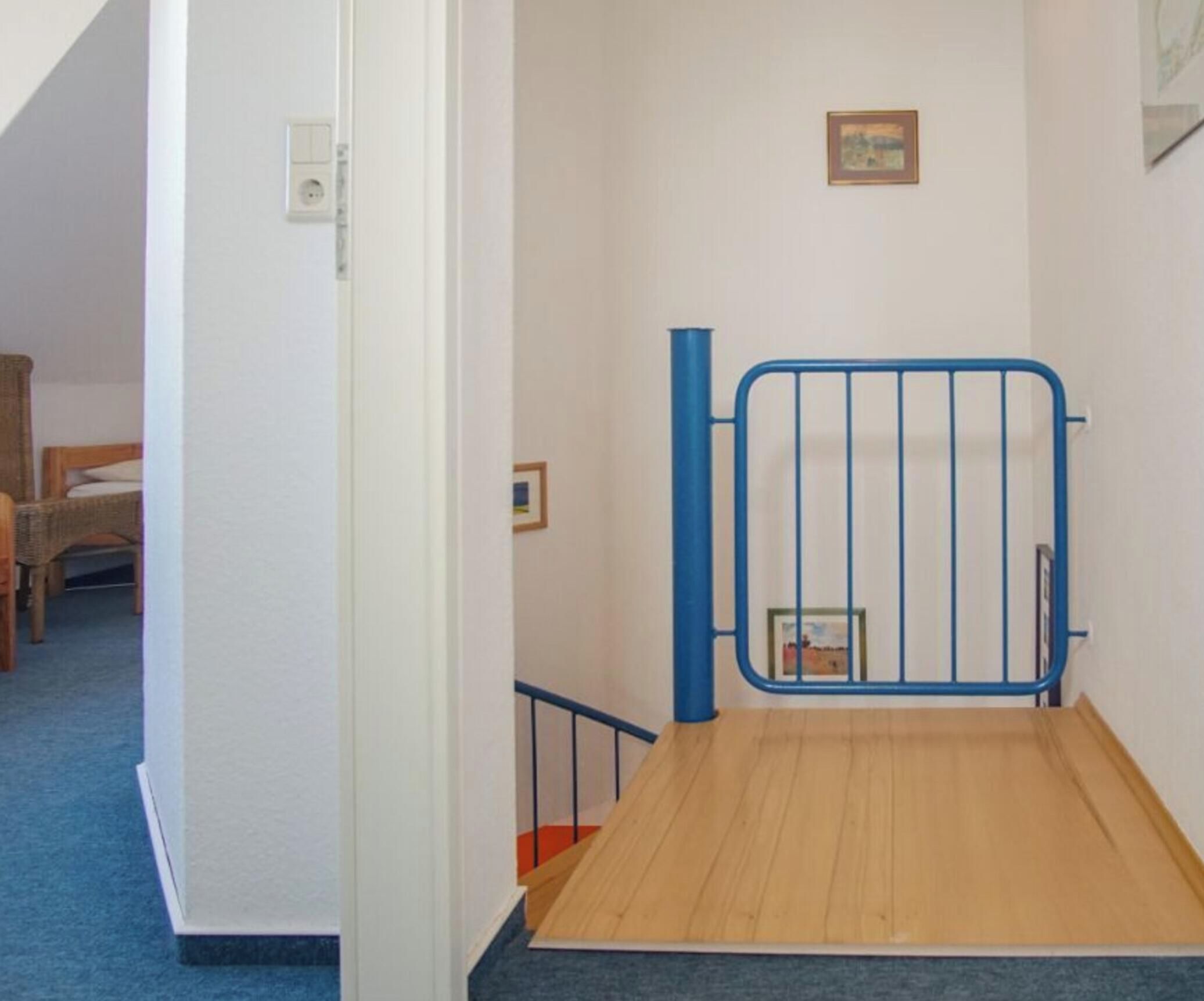Un escalier étroit avec une porte en métal bleue, un plancher en bois et une petite plateforme recouverte de moquette.