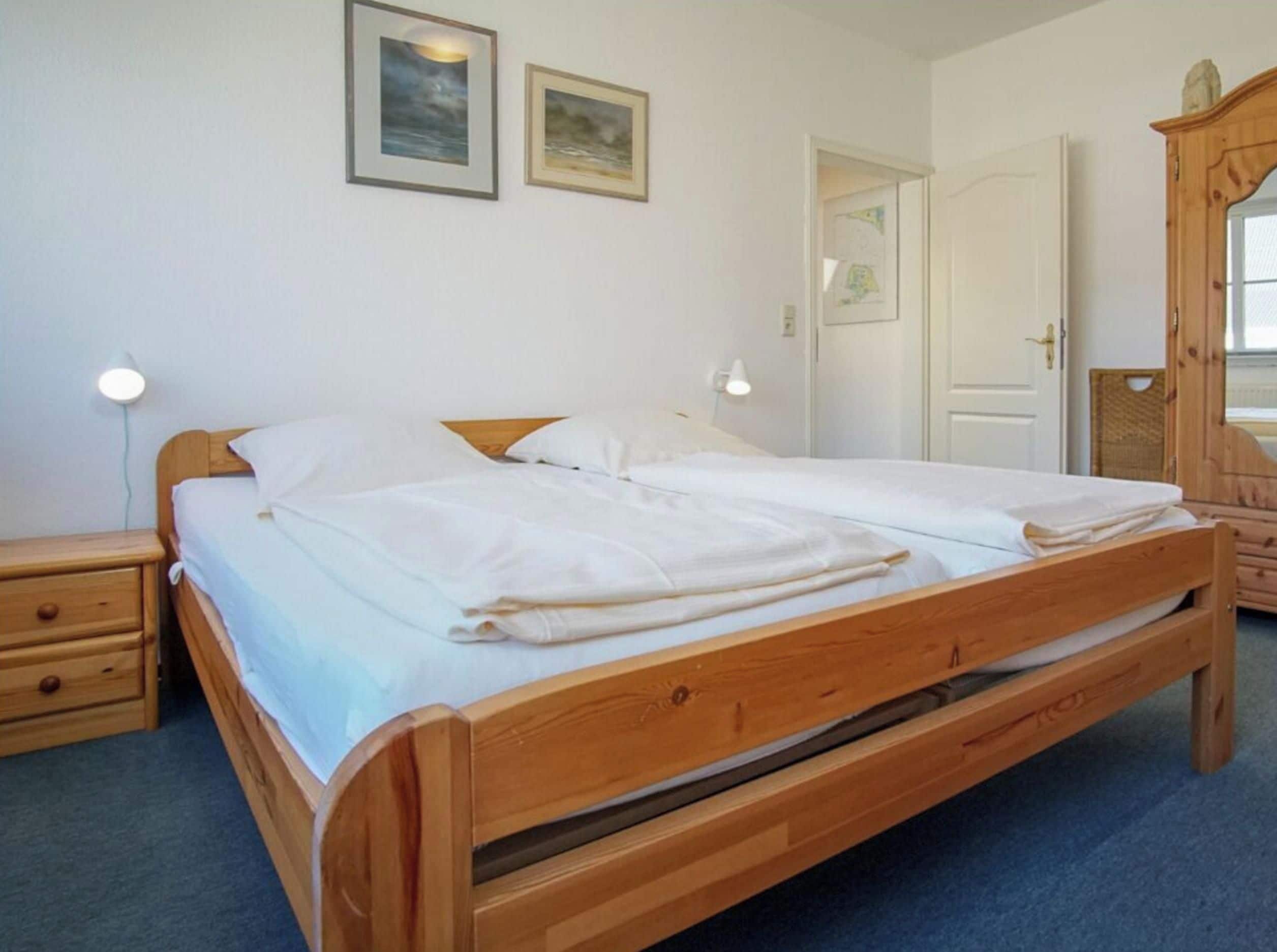 A room with a wooden bed, a nightstand, a dresser, and two wall-mounted lamps.