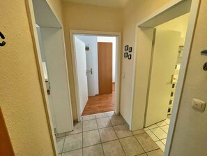 A narrow hallway with tiled flooring, white walls, and a wooden door leading to another room. - Villa Waldstrasse 03 (Heringsdorf)