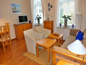 A living room with a TV, seating, a sofa, and a window with blinds. - Villa Waldstrasse 03 (Heringsdorf)