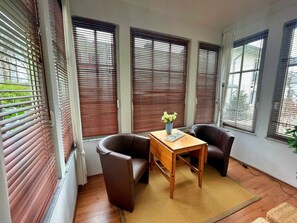 A room with a wooden table, two leather chairs, and a window with blinds. - Villa Waldstrasse 03 (Heringsdorf)