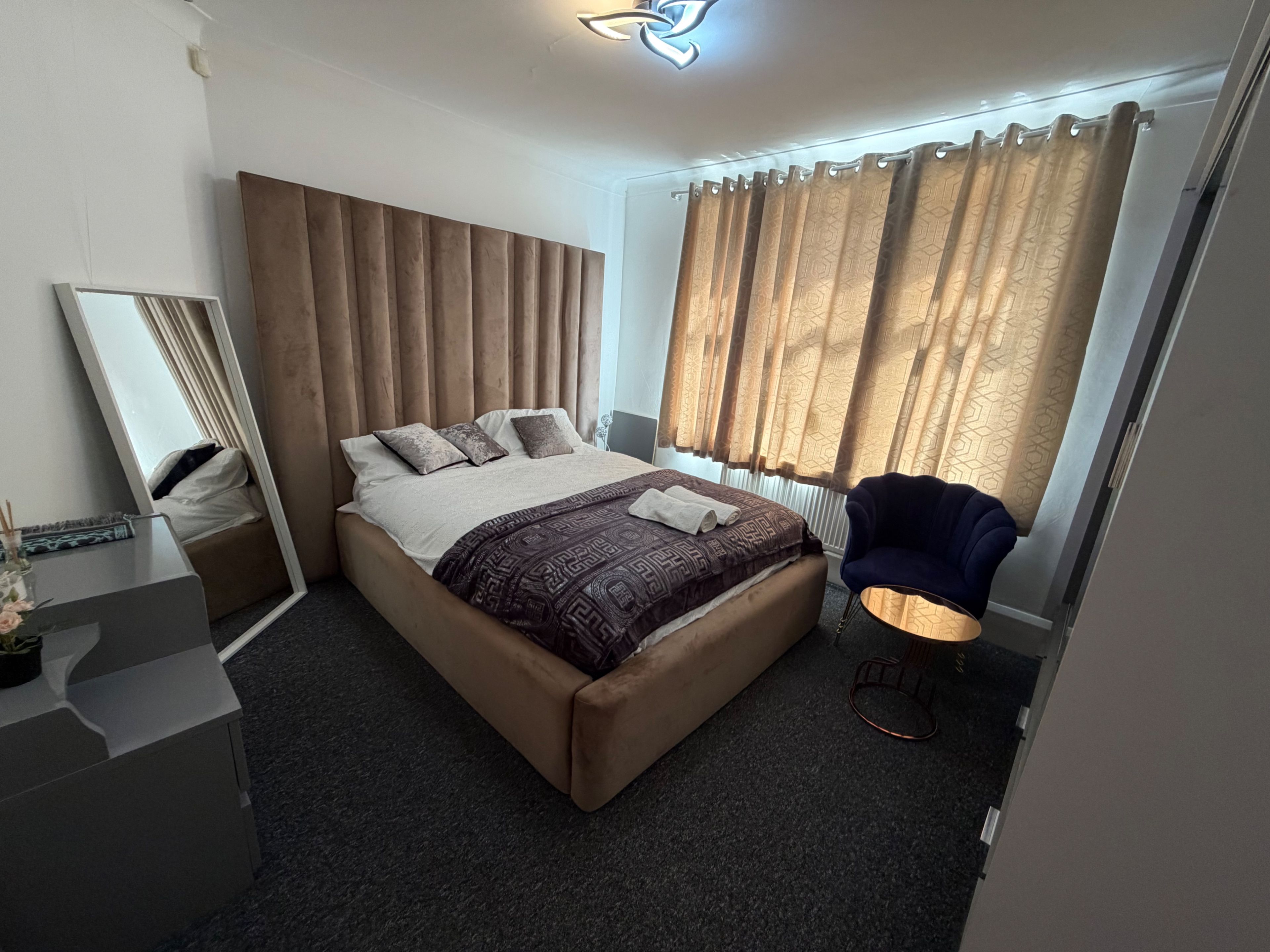 A modern hotel room with a large bed, a bedside table, a chair, and a window with curtains.