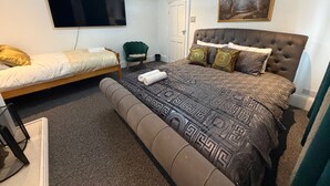 Un dormitorio con una cama grande, una cama más pequeña, un televisor, una silla y un cuadro en la pared.