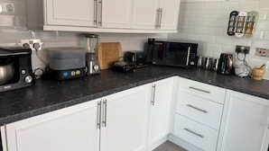 Una cocina moderna con armarios blancos, encimera negra y diversos electrodomésticos, incluyendo una licuadora, tostadora y microondas.