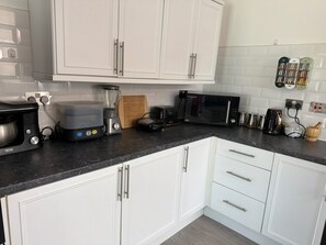 Eine moderne Küche mit weißen Schränken, einer schwarzen Arbeitsplatte und verschiedenen Geräten, darunter ein Mixer, ein Toaster und eine Mikrowelle.