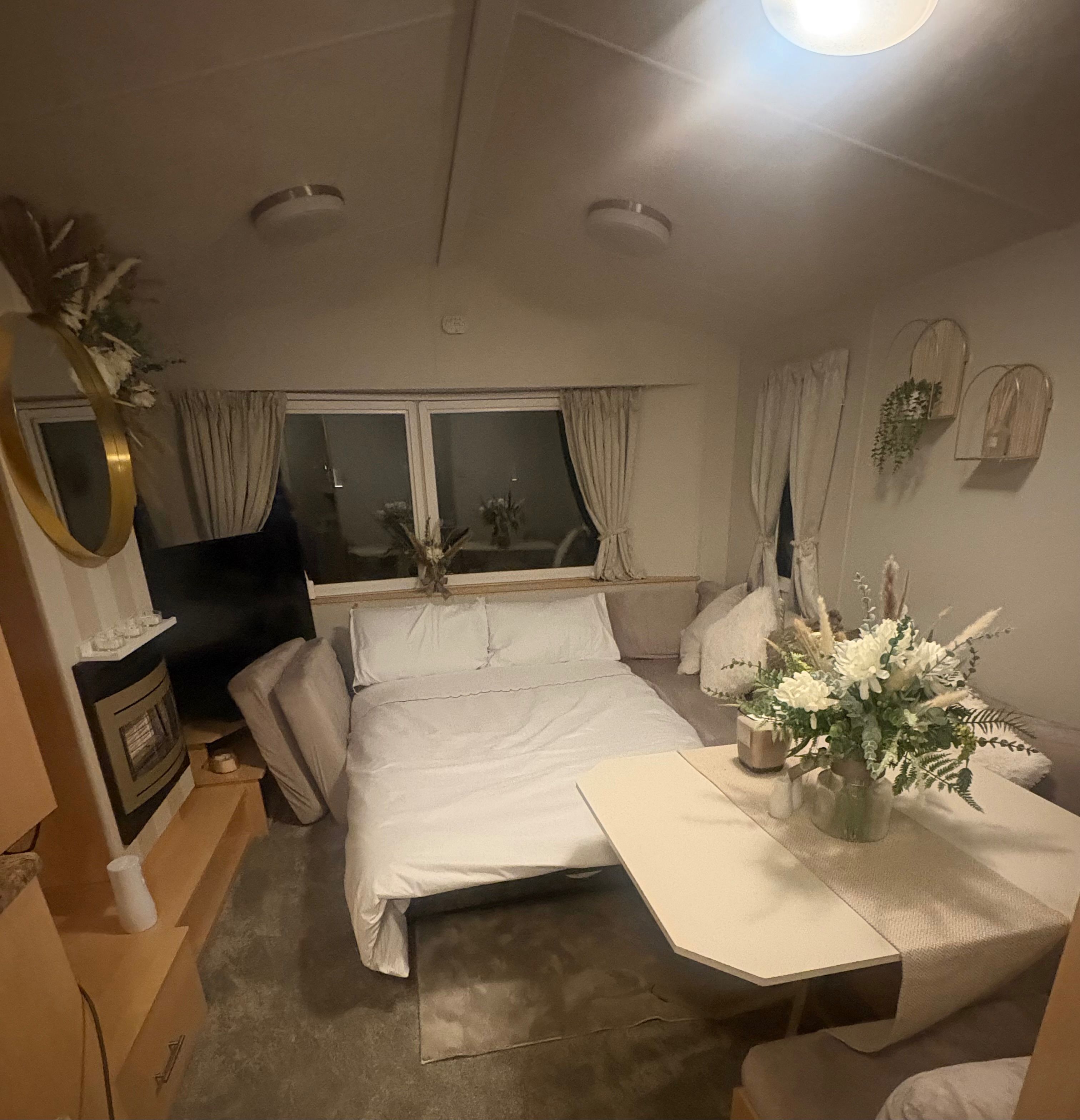 A bedroom with a bed, a bedside table, a dresser, a window with curtains, and a wall-mounted mirror.