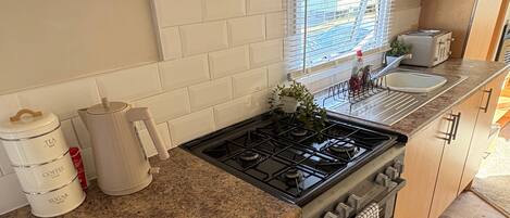 Una cocina compacta con estufa a gas, un lavamanos y un ventanal con persianas.