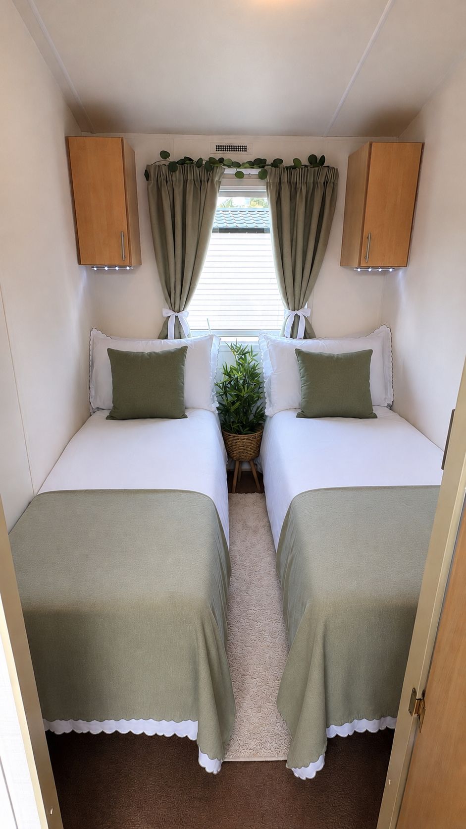 A compact RV bedroom with two beds, a small table, and a window with curtains.