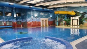 Una piscina interior con jacuzzi, toboganes y un mural en las paredes.