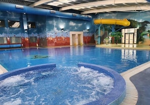 Ein Hallenbad mit Whirlpool, Rutschen und einem Wandgemälde an den Wänden.