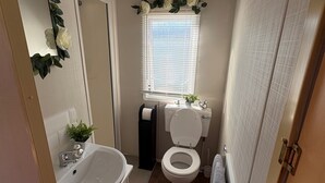 Un baño pequeño con lavamanos, inodoro y ventana con persianas.