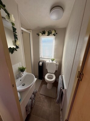 Ein kleines Badezimmer mit einem weißen Waschbecken, Toilette und einem Fenster mit Jalousien.