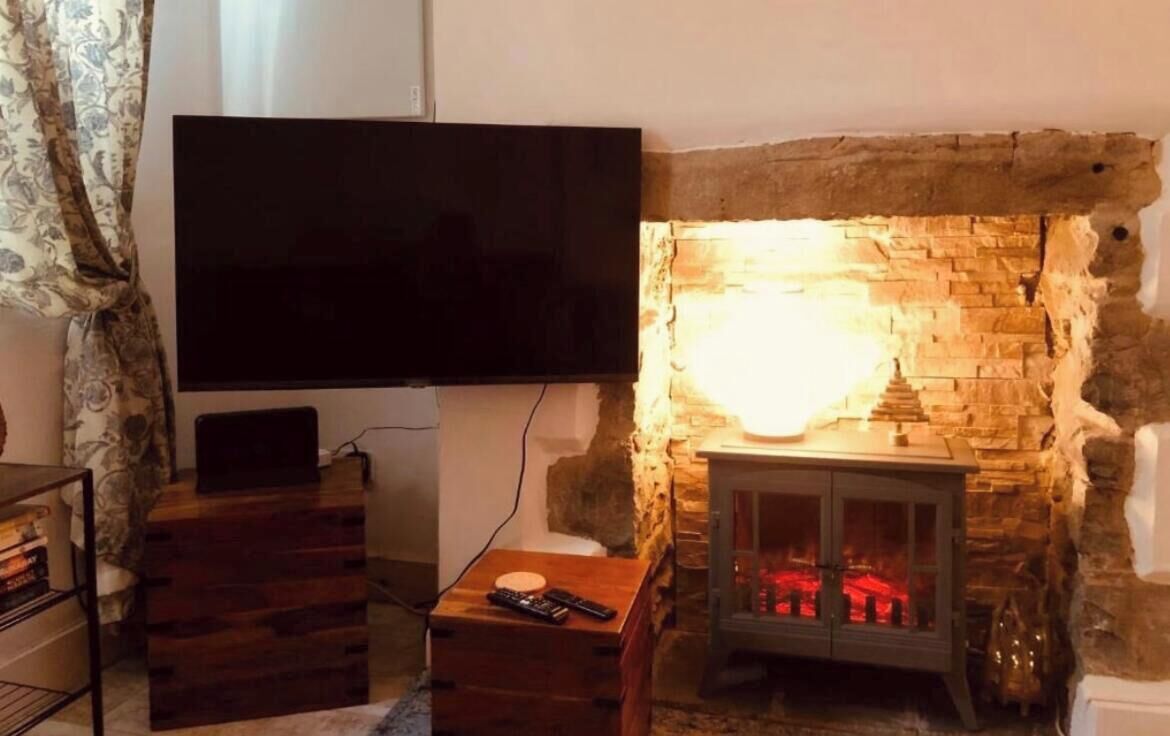 A living room with a stone fireplace, a flat-screen TV mounted on the wall, and a small wooden table with a remote control.