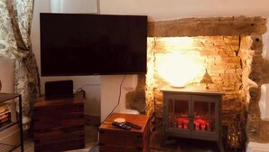 Un salon doté d’une cheminée en pierre, d’un téléviseur à écran plat fixé au mur et d’une petite table en bois sur laquelle repose une télécommande.