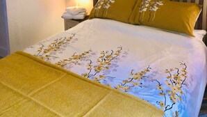 Un lit bien fait, recouvert d’une couvre-lit à motifs floraux, avec une tête de lit en bois et un lustre suspendu.