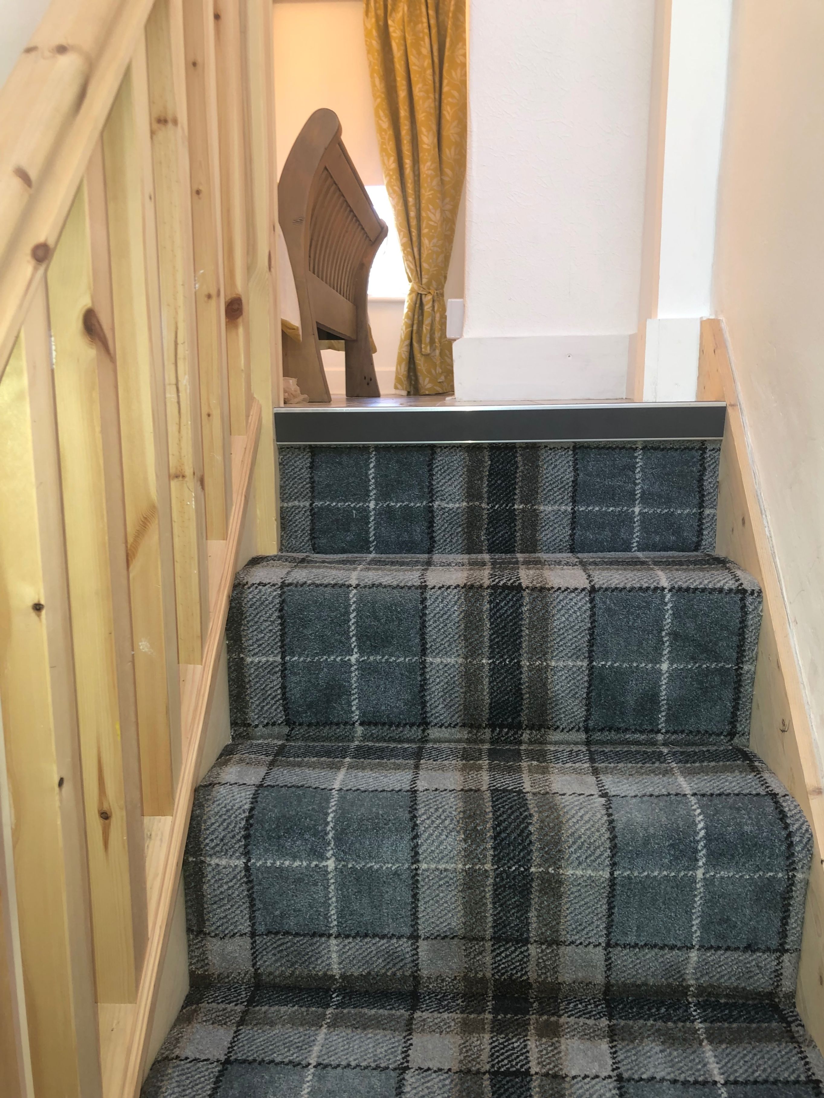 A staircase with a checkered carpet and wooden handrail.