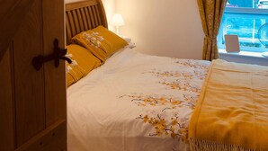 Een slaapkamer met een bed, een kroonluchter, een raam met gordijnen en een deur.