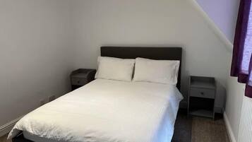 Ein Einzelbett mit dunklem Kopfteil in einem Zimmer mit weißen Wänden und geneigter Decke. An jeder Seite des Bettes befinden sich zwei Nachttische.