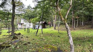 Mökki, joka on rakennettu maalaismaisessa tyylissä ja sijaitsee metsäisen alueen keskellä, lähellä niittyä ja pientä lampea.