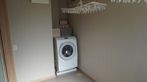 A laundry area with a washing machine, a drying rack, and a small shelf with baskets.