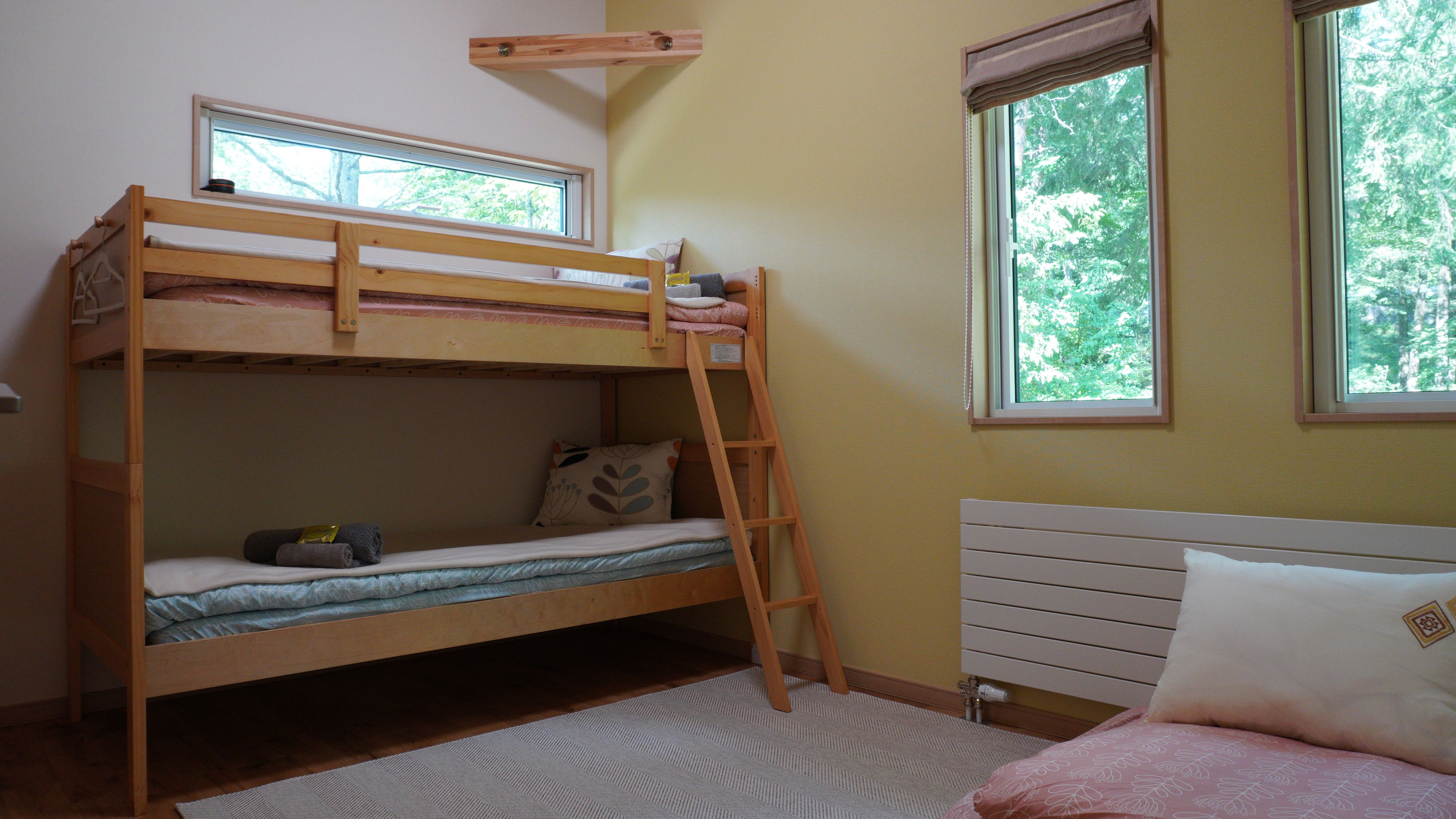 A bunk bed with a ladder, a single bed with a headboard, and two windows with curtains.