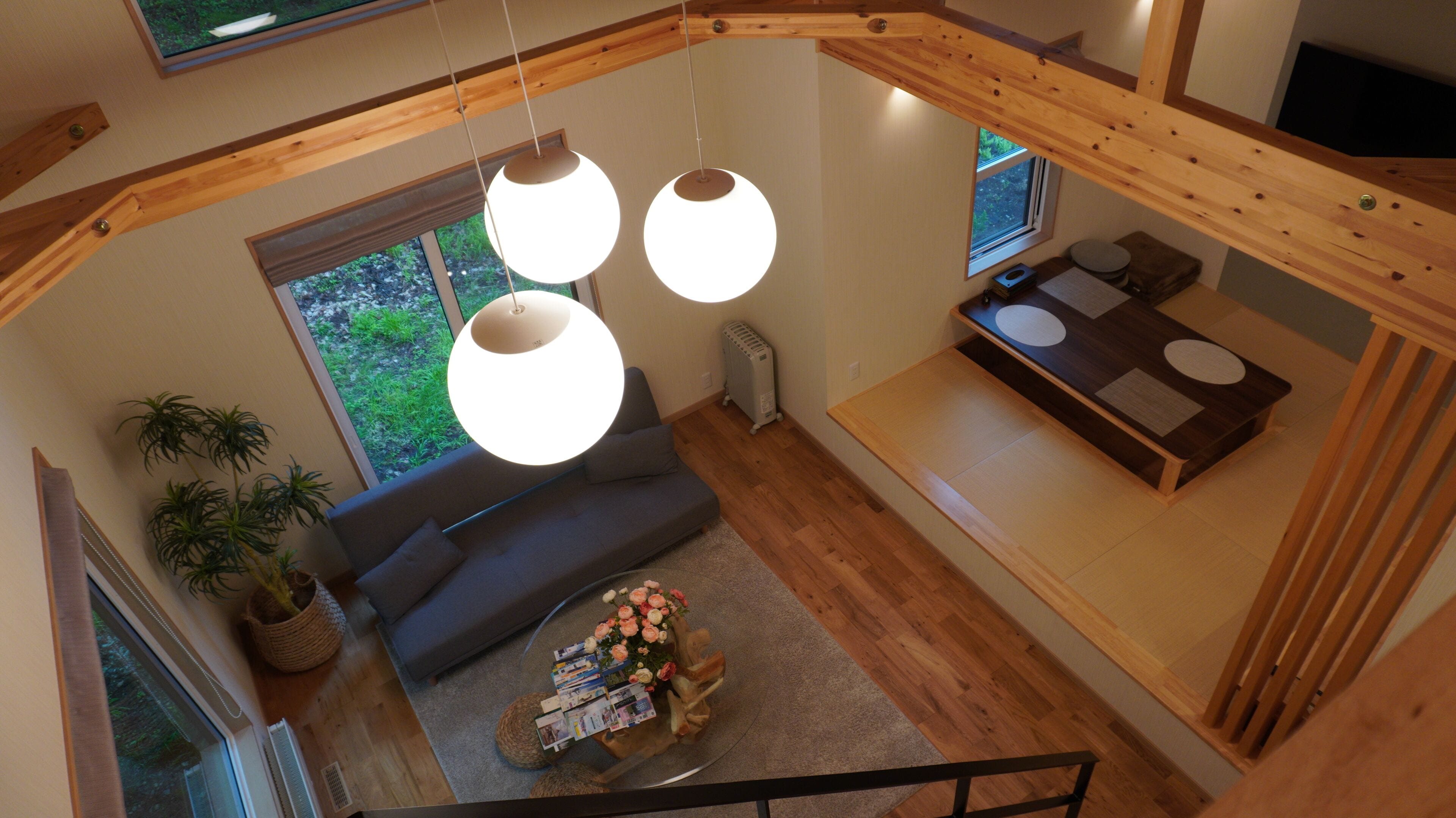 Un interior moderno con diseño estilo loft, que presenta una escalera de madera, un sofá gris y una zona de comedor con mesa de madera.