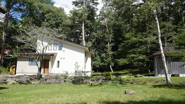 A modern house with a white exterior, surrounded by a natural landscape with trees and rocks.